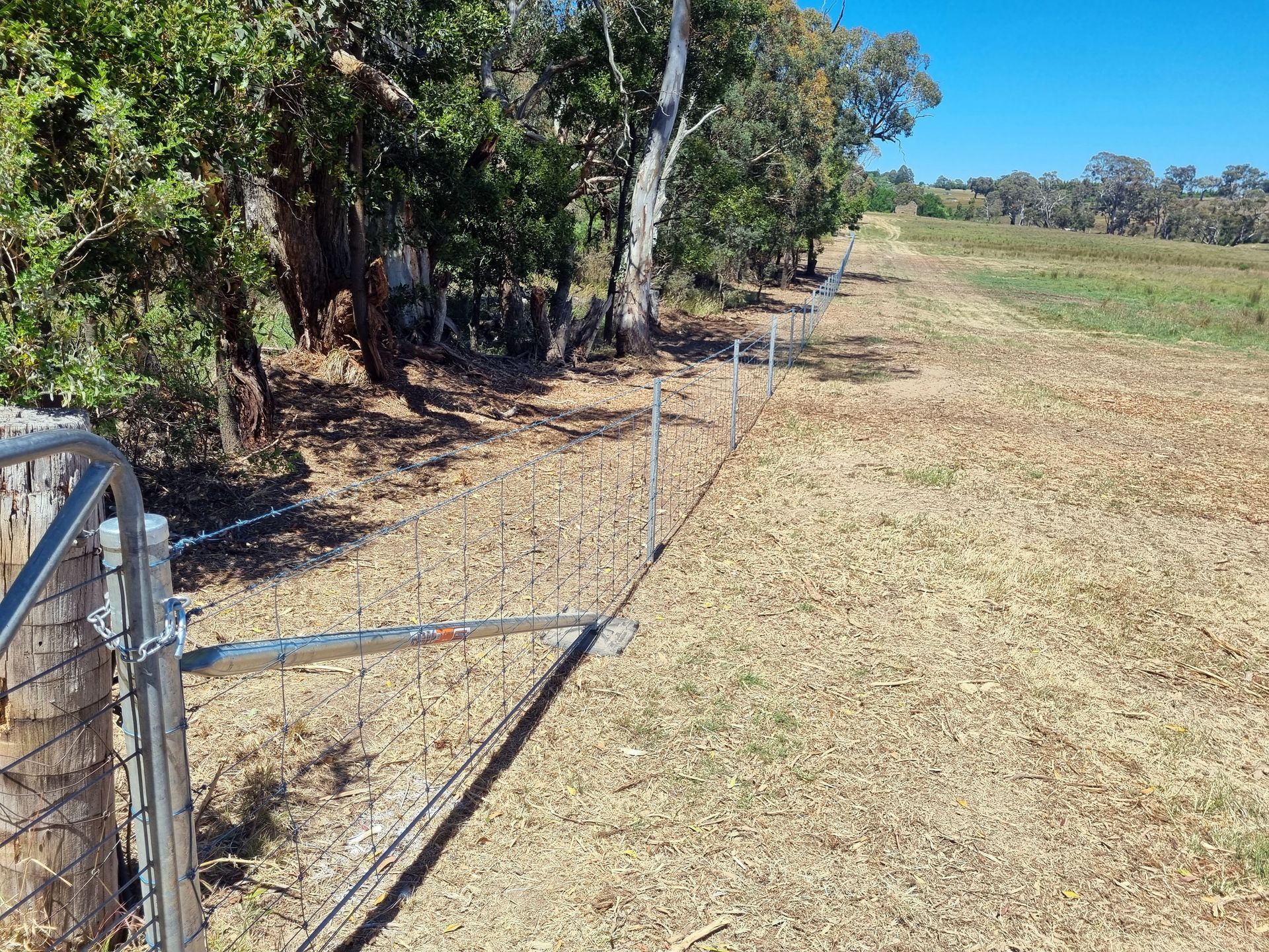 A small white building behind a chain link fence in a field.— Ettles Rural Fencing in Alfredton, VIC