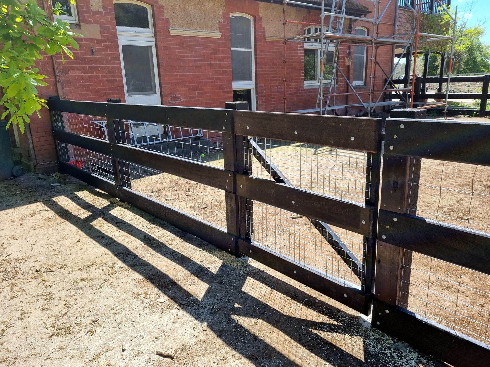 A wooden fence surrounds a dirt field with trees in the background.— Ettles Rural Fencing in Alfredton, VIC