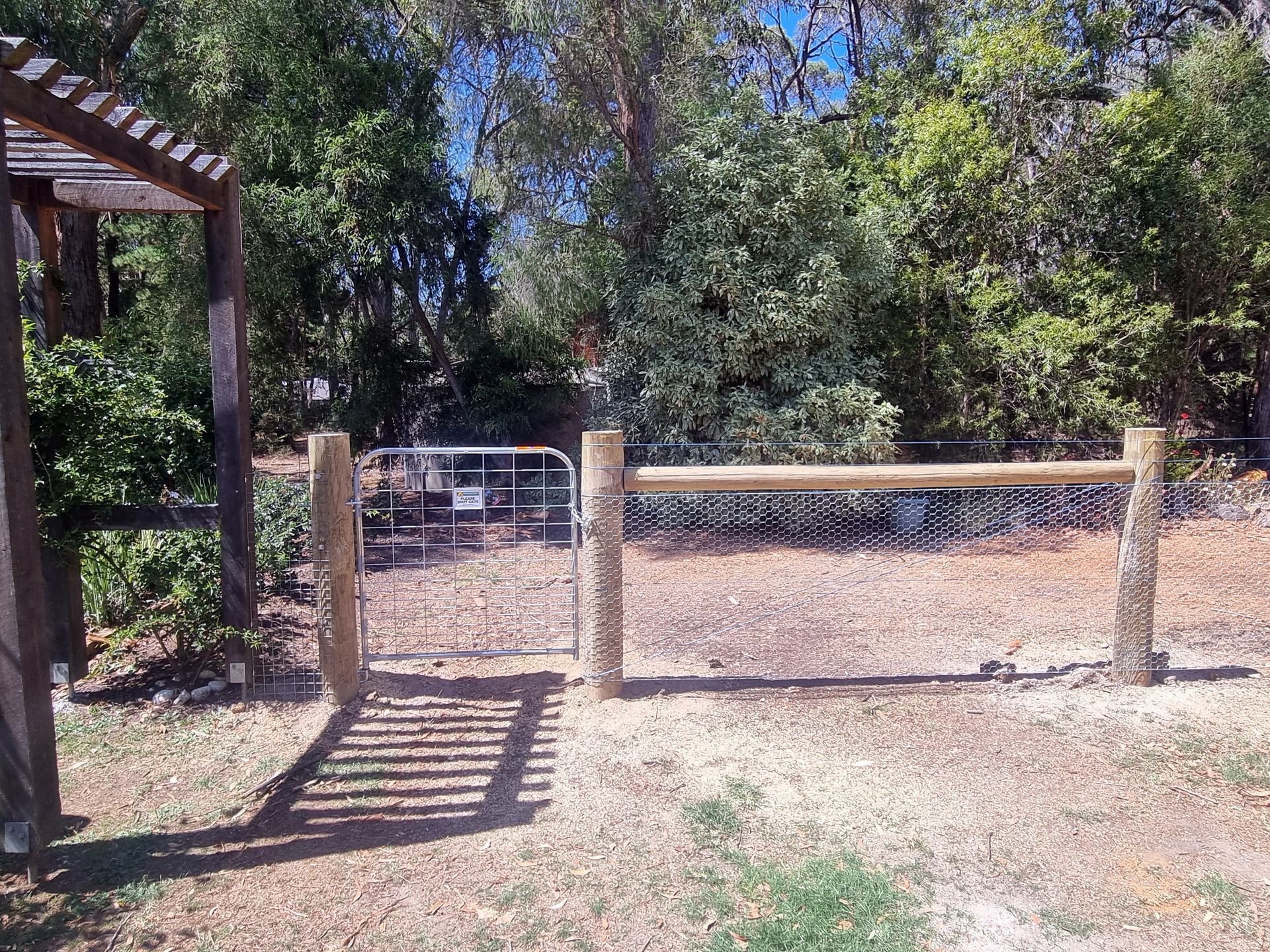 A wooden fence with a metal gate in front of a building.— Ettles Rural Fencing in Alfredton, VIC