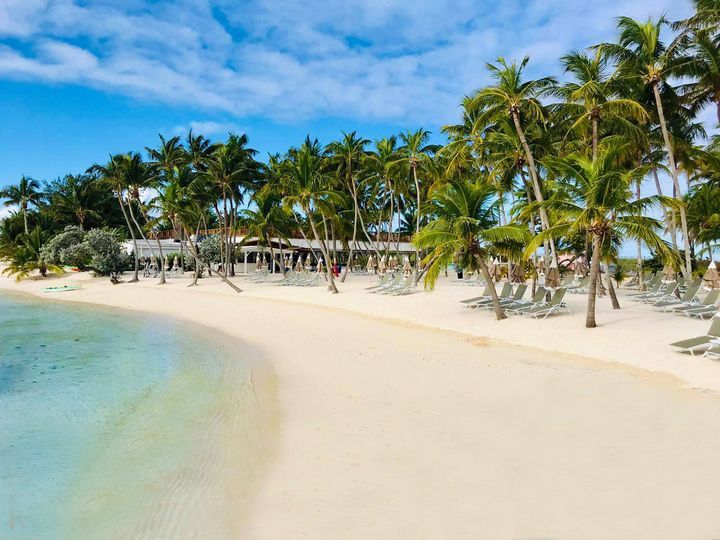 Beach with white sand, turquoise water, palm trees, and a beachfront building under a blue sky.