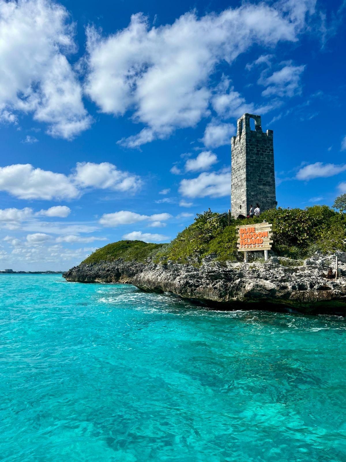 Stone tower on a rocky island in turquoise water under a bright blue sky with fluffy clouds.
