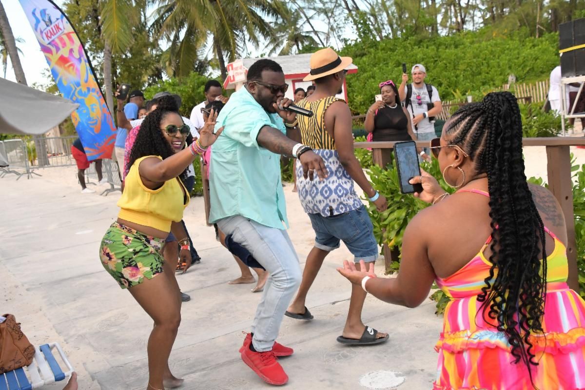 A singer performs outdoors at a beach party. Several people dance and record with their phones.
