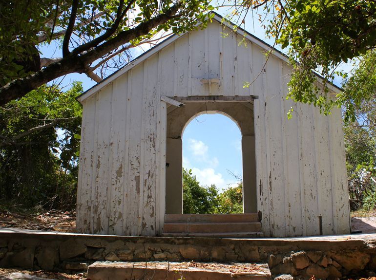 White, weathered building with an arched opening framing a bright blue sky.