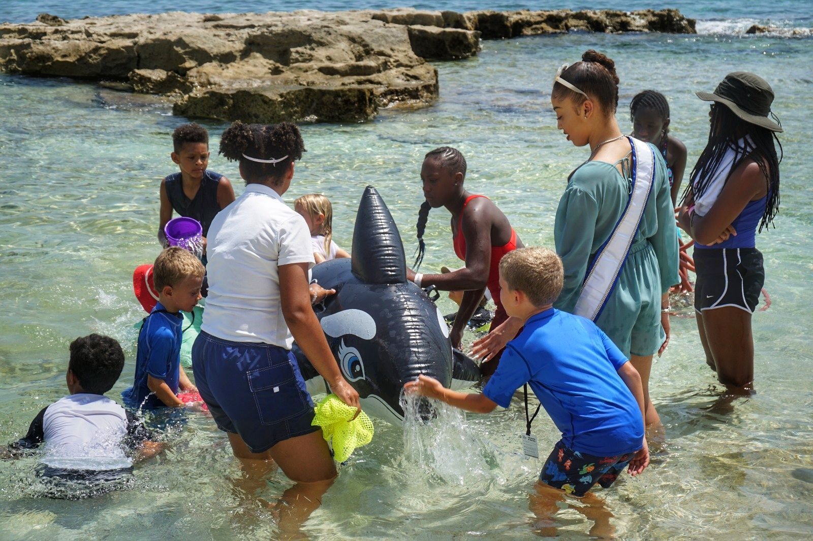 Group of children and two adults smiling and posing in front of a wooden wall; 