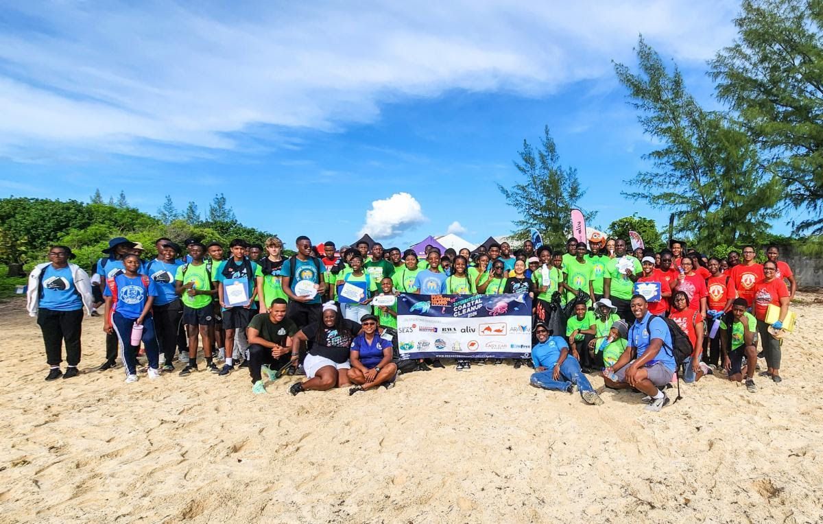 Group of people on a beach, smiling. Many wear colorful shirts. Clear sky, beach in the Bahamas.