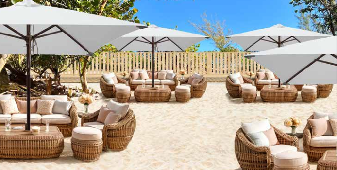 Beach lounge with woven furniture, white umbrellas, and beige cushions.