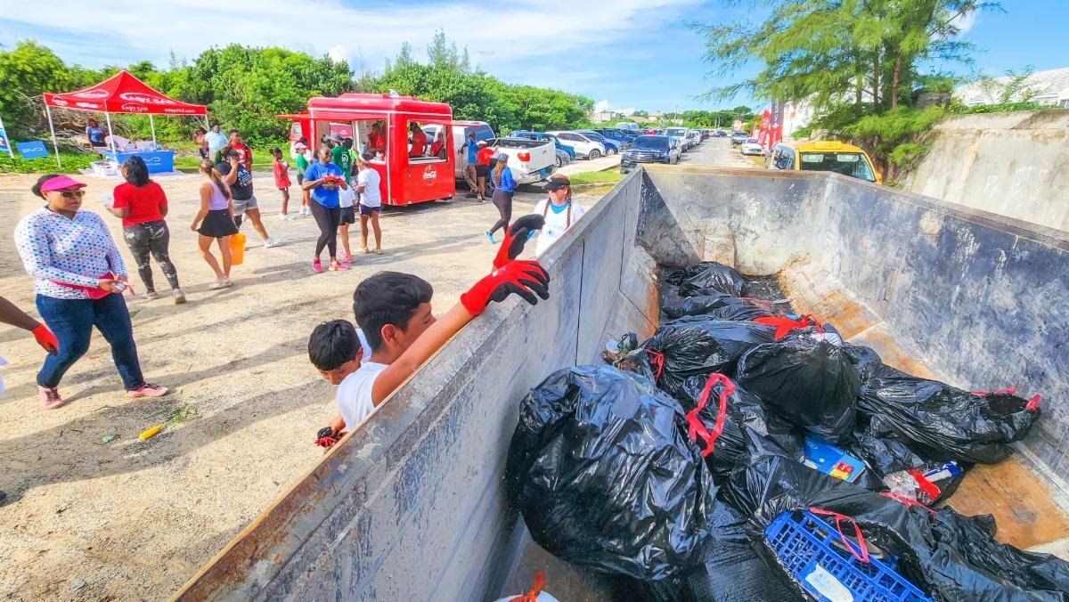 People cleaning up litter at a beach; boy reaching into a dumpster filled with black bags.
