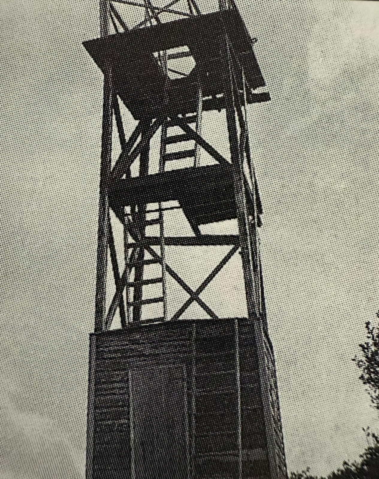 A tall stone tower on a small, green island, with turquoise water and a boat in the distance.
