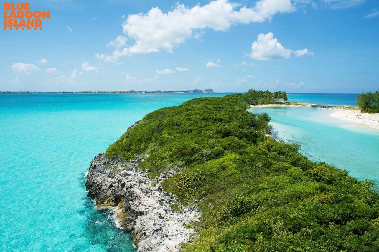 A narrow, green, land strip in turquoise water under a blue sky with fluffy clouds.