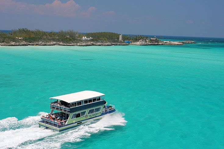 A two-story boat speeding across turquoise water toward a small island under a clear blue sky.