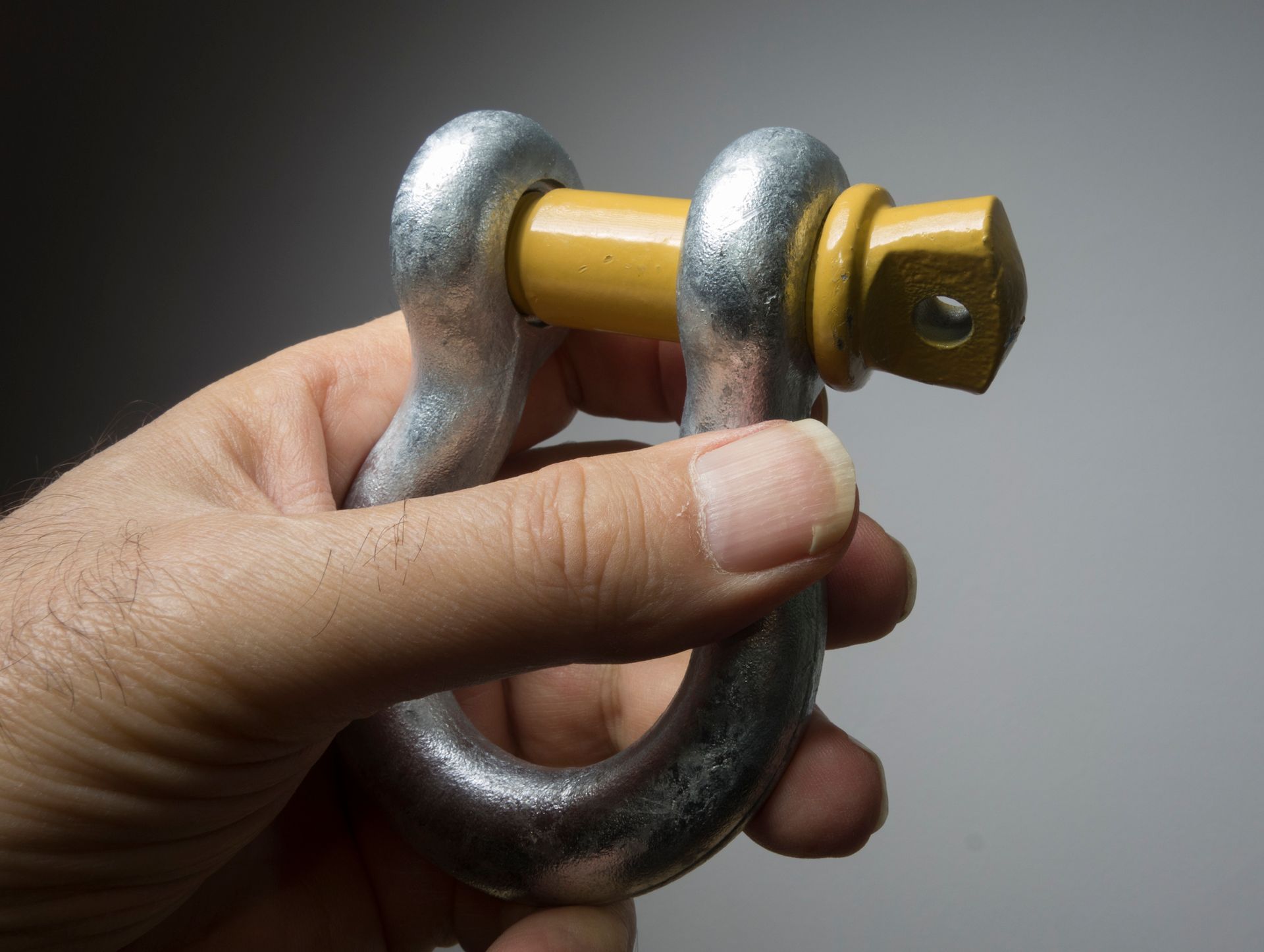 A person is holding a metal shackle with a yellow handle.