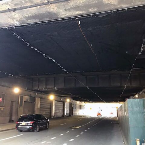 A car is driving under a bridge in a tunnel.