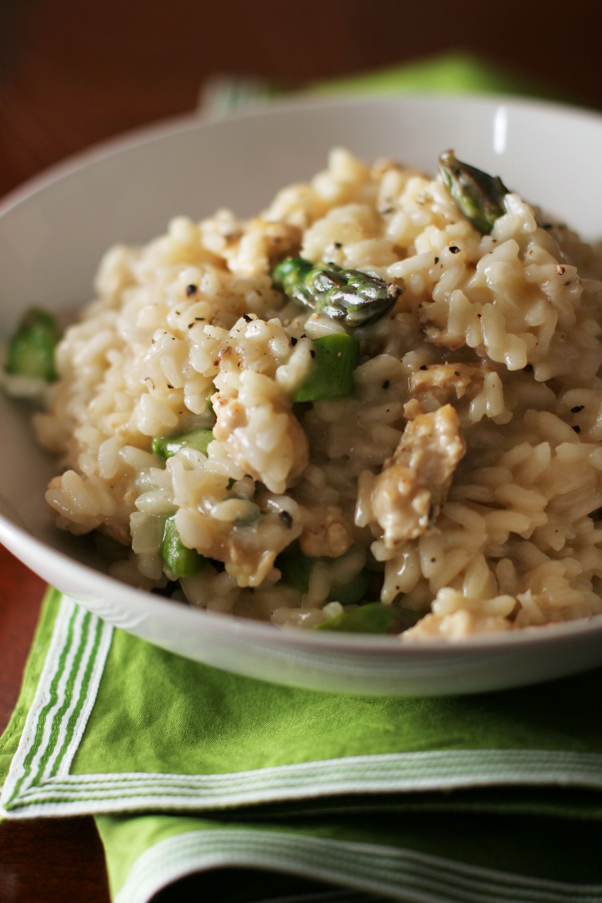 Una ciotola di risotto con asparagi e pollo su un tovagliolo su un tavolo.