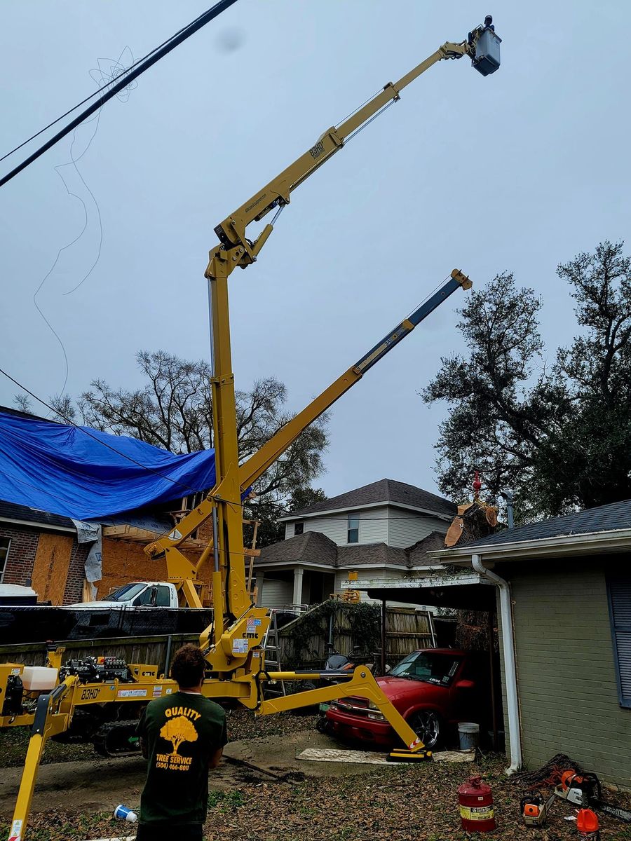 A person in a green shirt operates a yellow crane lift elevated over a residential yard with a house and a blue tarp.