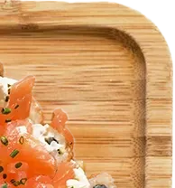 Gros plan sur le coin arrondi d'un plateau en bambou contenant du saumon et une garniture blanche.