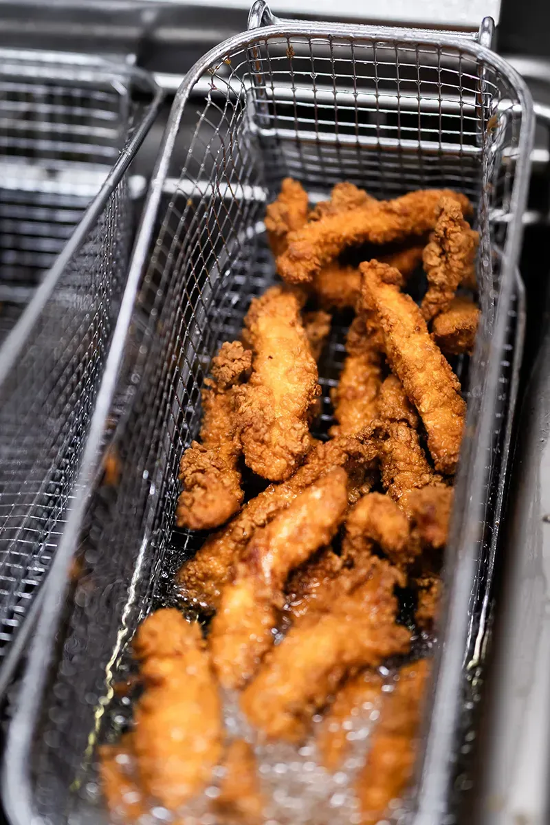 Des filets de poulet frits dans un panier métallique, immergés dans de l'huile bouillonnante.