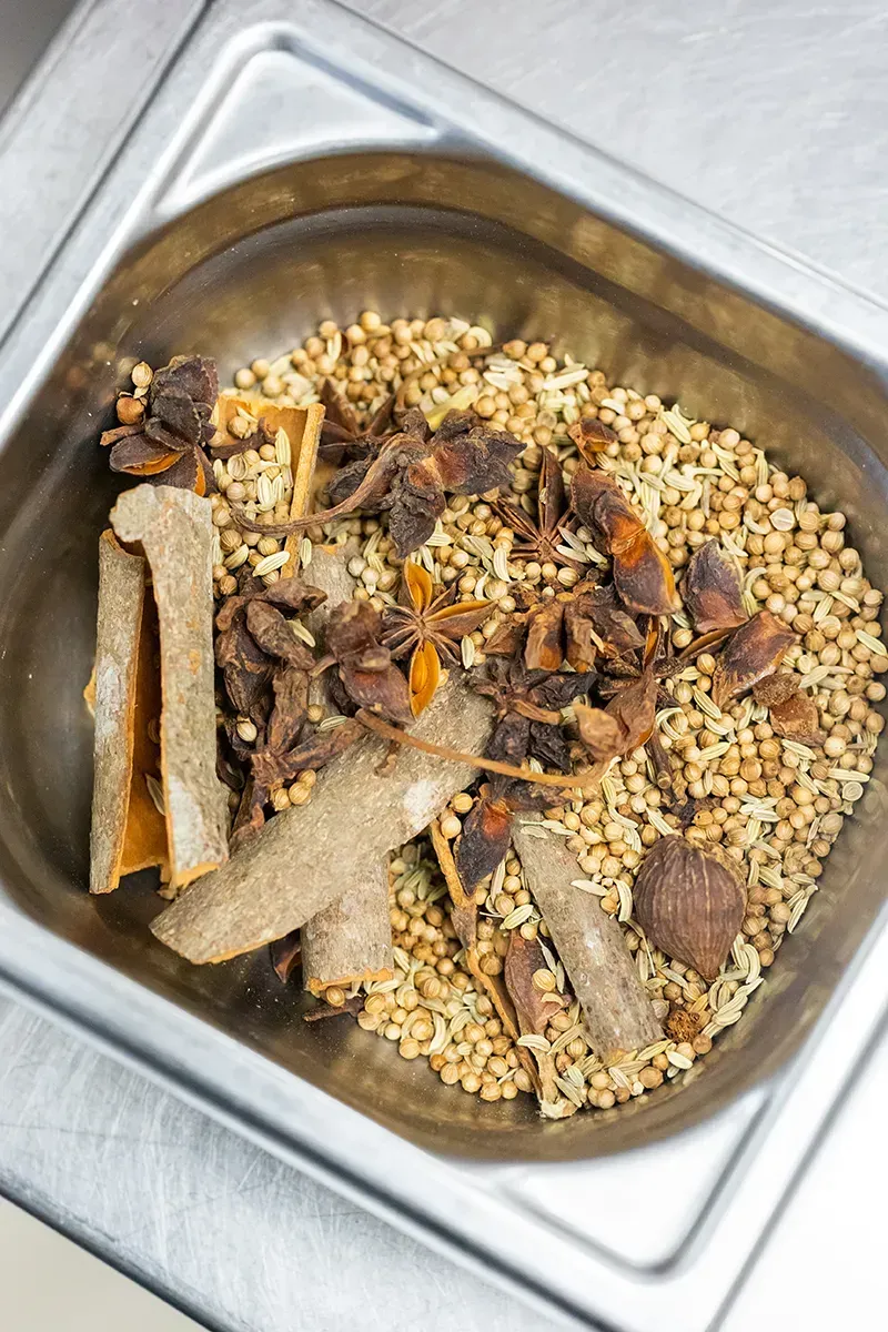 Récipient métallique contenant des épices : anis étoilé, bâtons de cannelle, grains de poivre et autres épices entières.