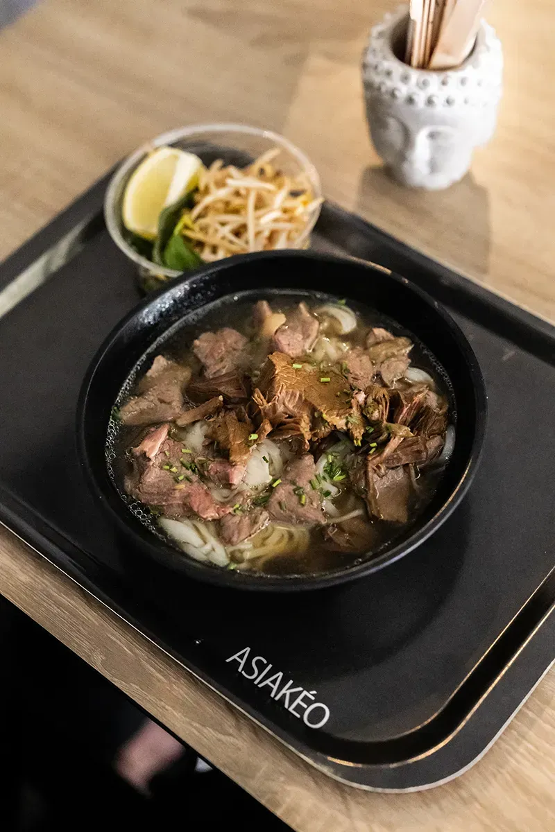 Bol de pho au bœuf et aux nouilles, servi avec des germes de soja et du citron vert sur un plateau.