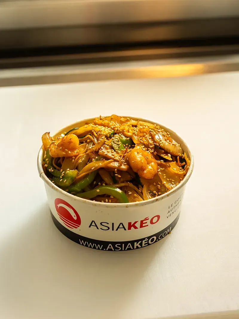 Bol alimentaire Asia Keo garni de crevettes, poivrons et oignons. Bol en papier blanc et noir avec logo.