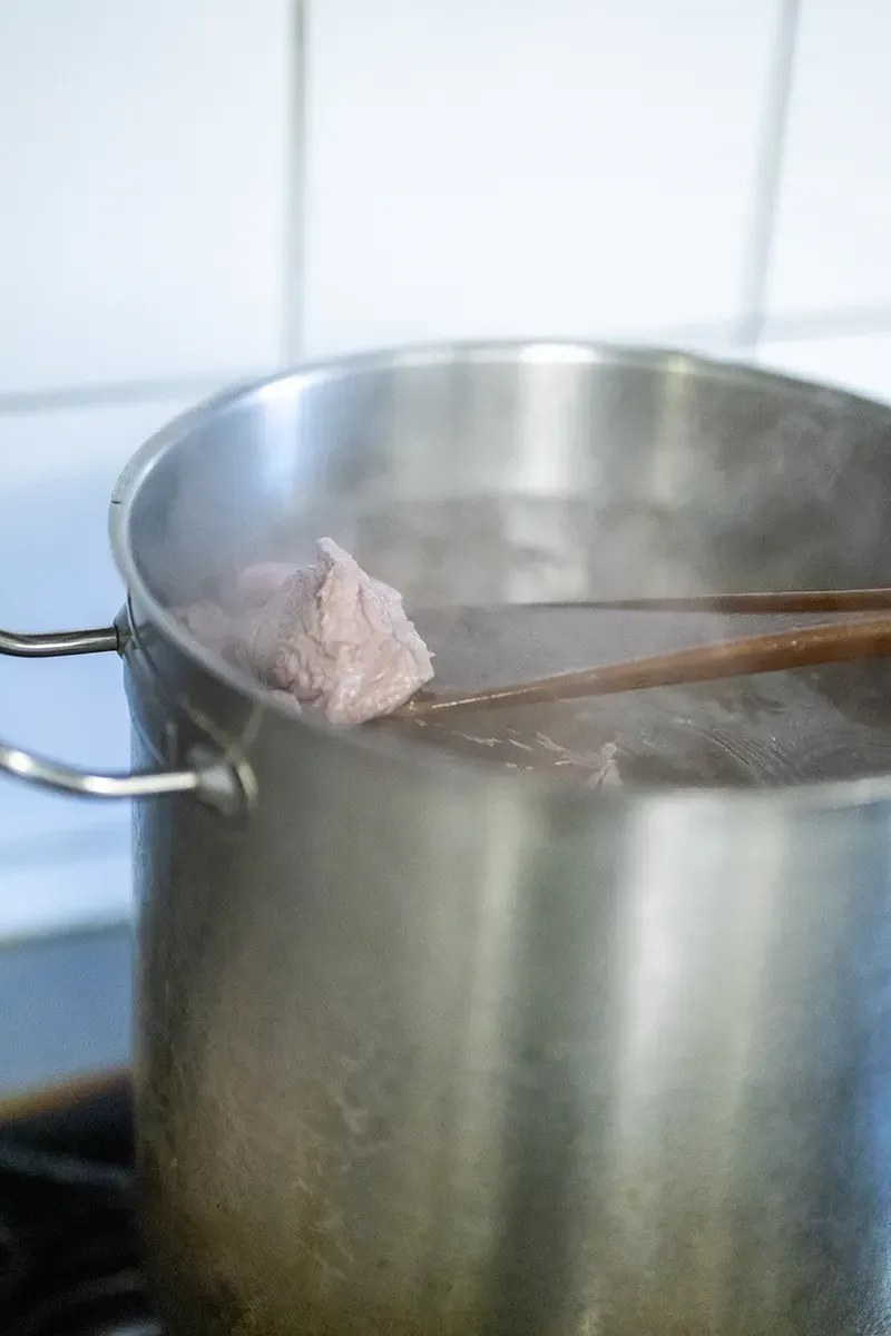 Une casserole d'eau bouillante d'où s'échappe de la vapeur et un objet rose tenu par des baguettes en bois.