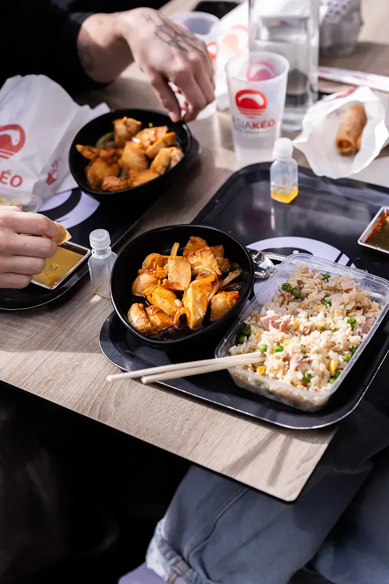 Deux personnes mangent de la nourriture asiatique en plein air : crevettes, riz frit, rouleaux de printemps et sauces.