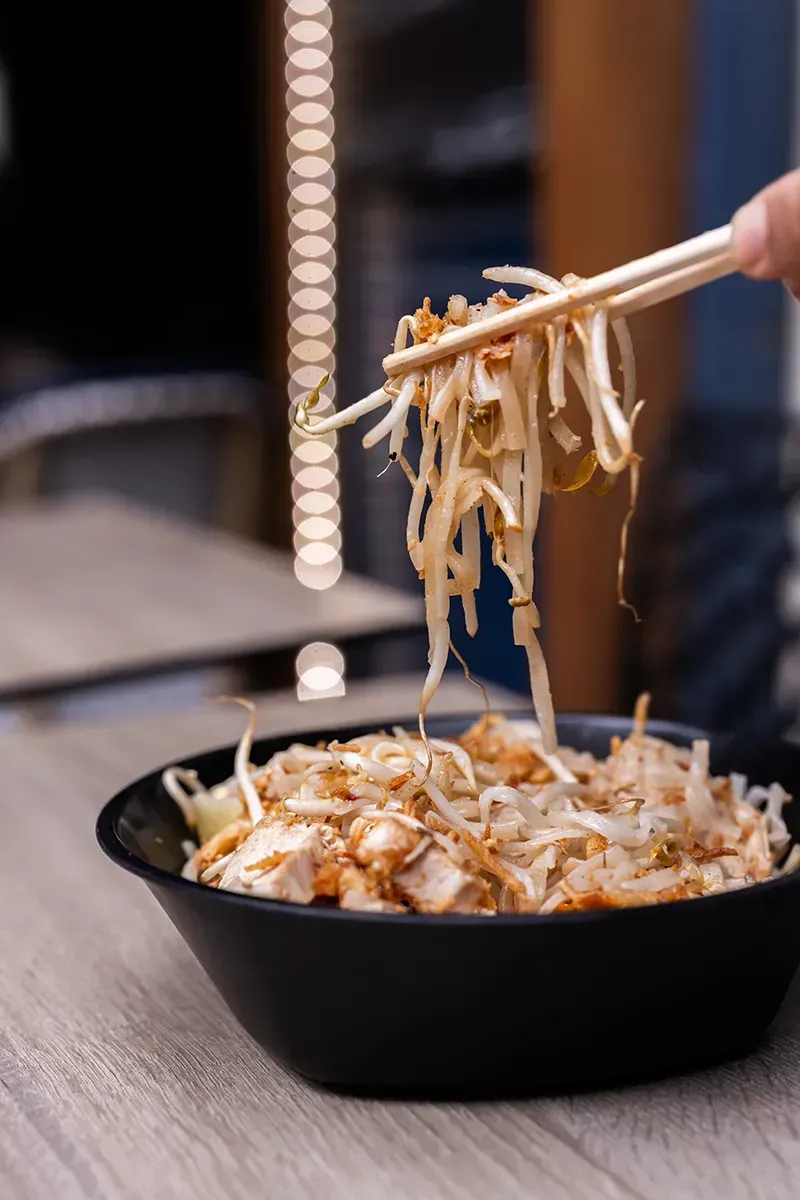Des nouilles et des germes de soja sont sortis d'un bol noir à l'aide de baguettes ; vue rapprochée.