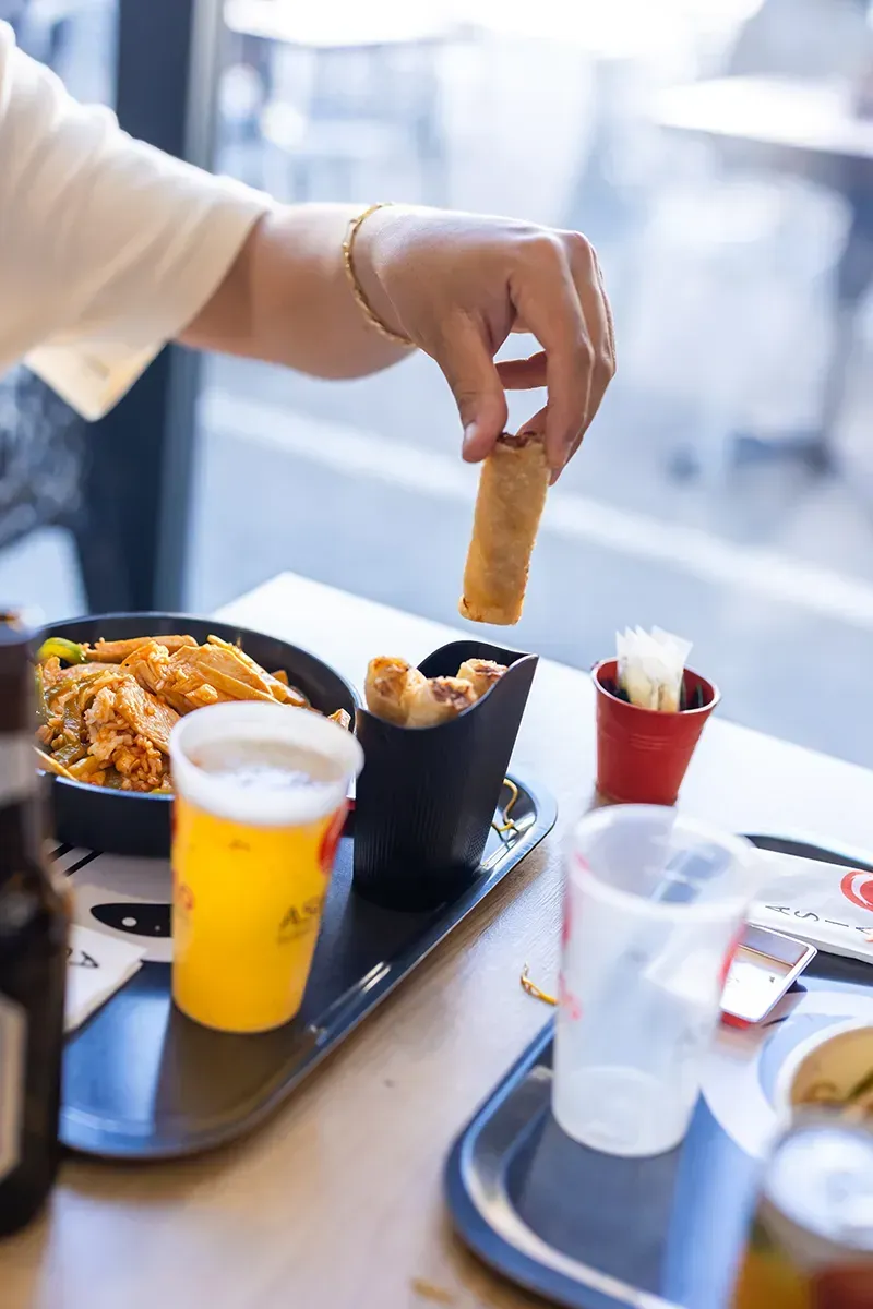 Une personne trempe un rouleau de printemps dans une sauce, d'autres aliments et boissons se trouvent sur la table.