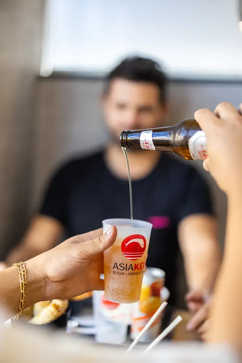 De la bière est versée d'une bouteille dans un gobelet en plastique transparent, devant un homme.