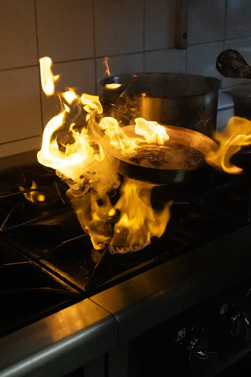 Des flammes jaillissent d'une poêle sur le feu, avec une casserole en arrière-plan.