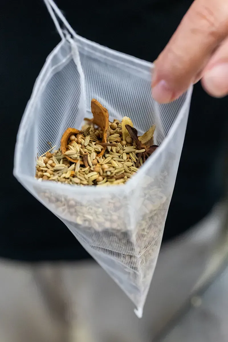 Main tenant un sachet de thé en filet rempli d'herbes et d'épices séchées.