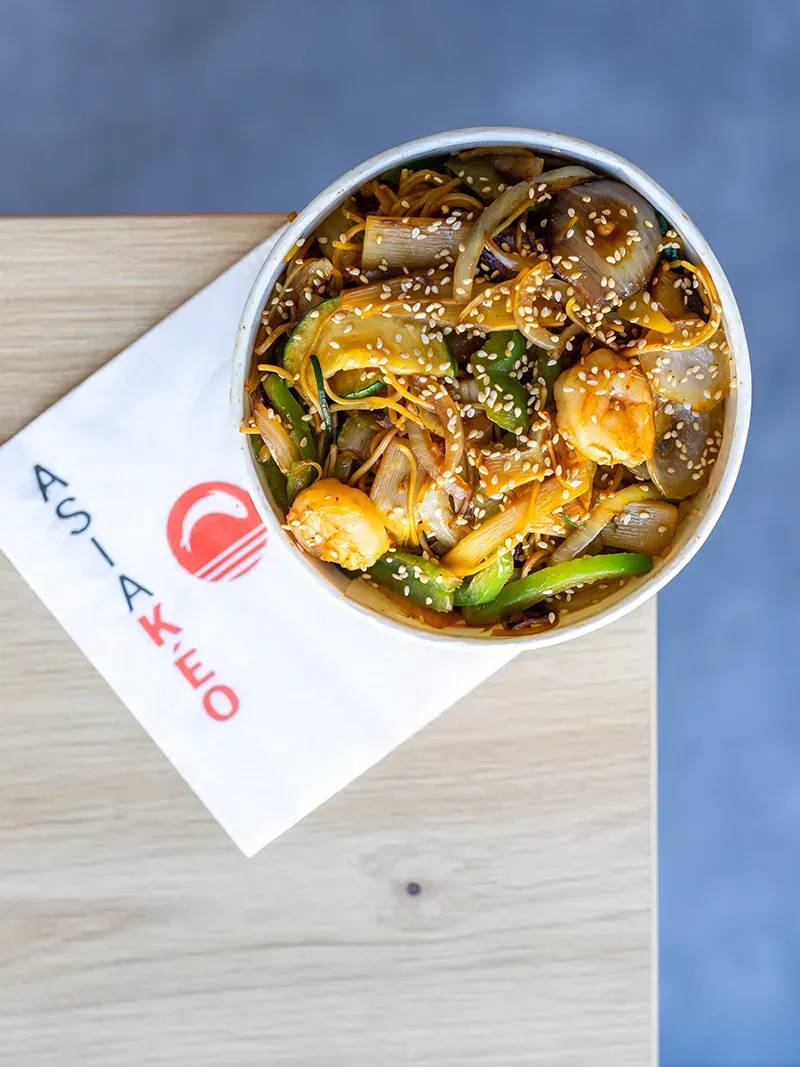 Bol de nourriture asiatique avec légumes et crevettes sur une serviette à logo.