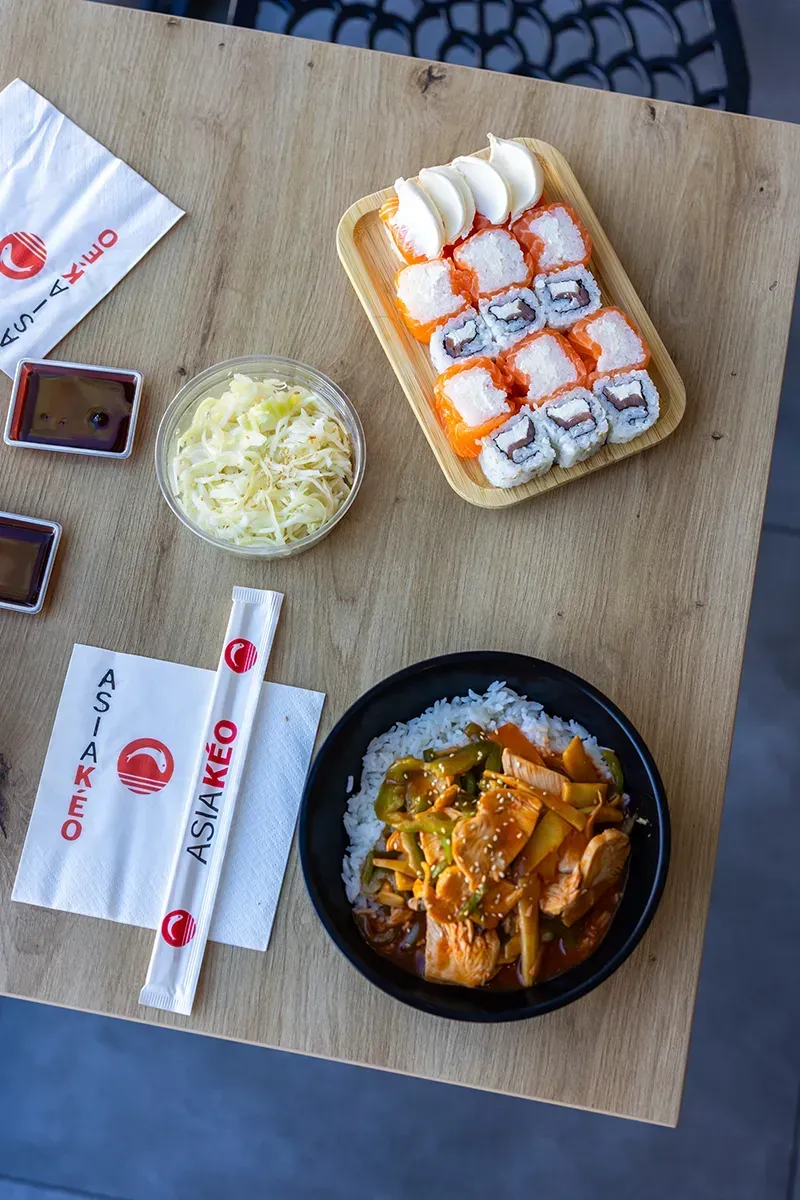 Des rouleaux de sushi, un bol de riz et des accompagnements disposés sur une table en bois.