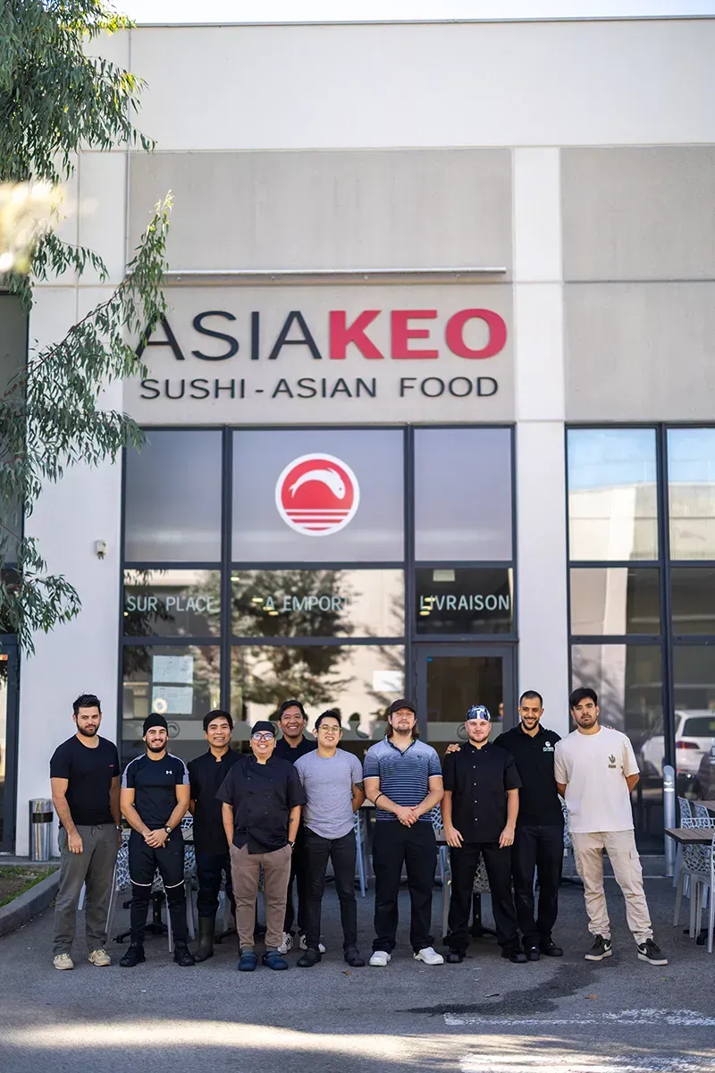 Groupe de serveurs devant le restaurant Asia Keo. Logo rouge au-dessus du texte « Sushi - Cuisine asiatique ».