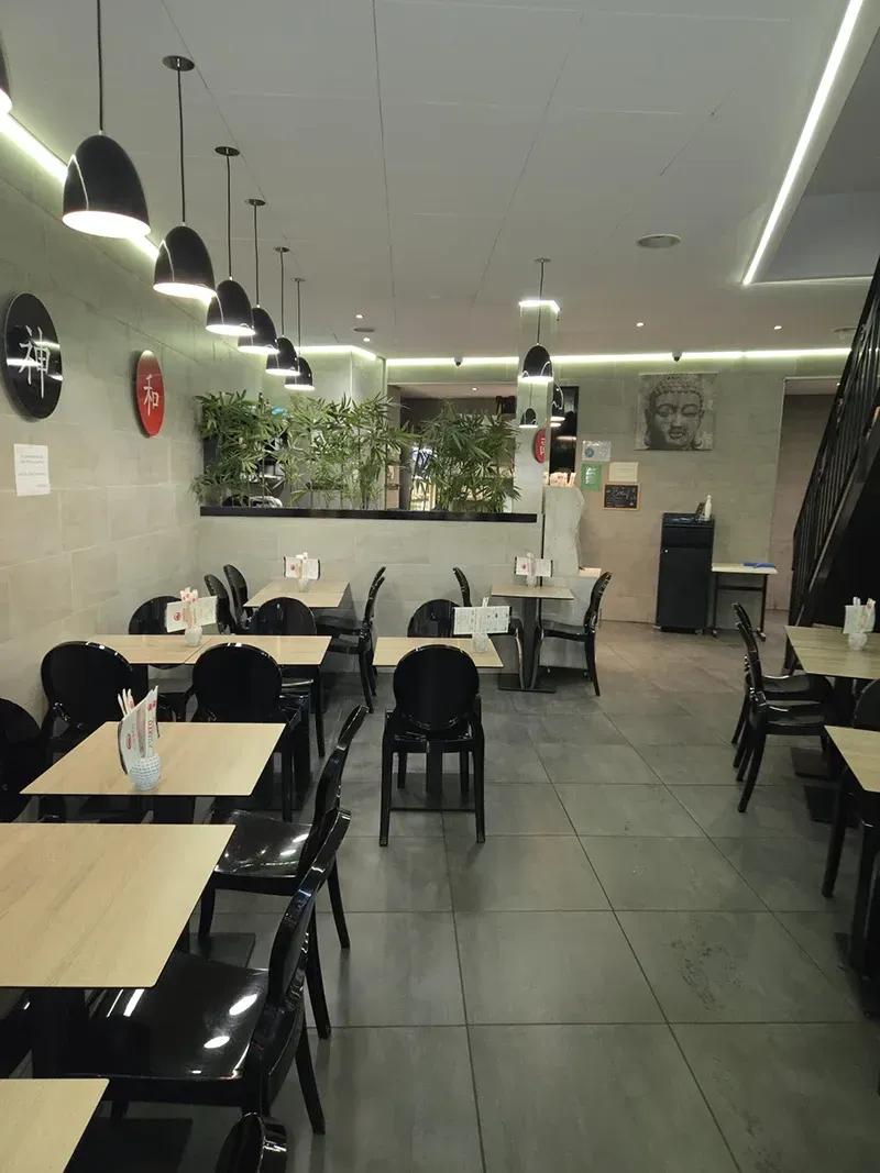 Intérieur de restaurant avec tables en bois, chaises noires et paravent en bambou.