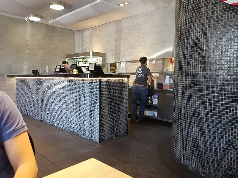 Comptoir de restaurant avec mosaïque, employés et client.