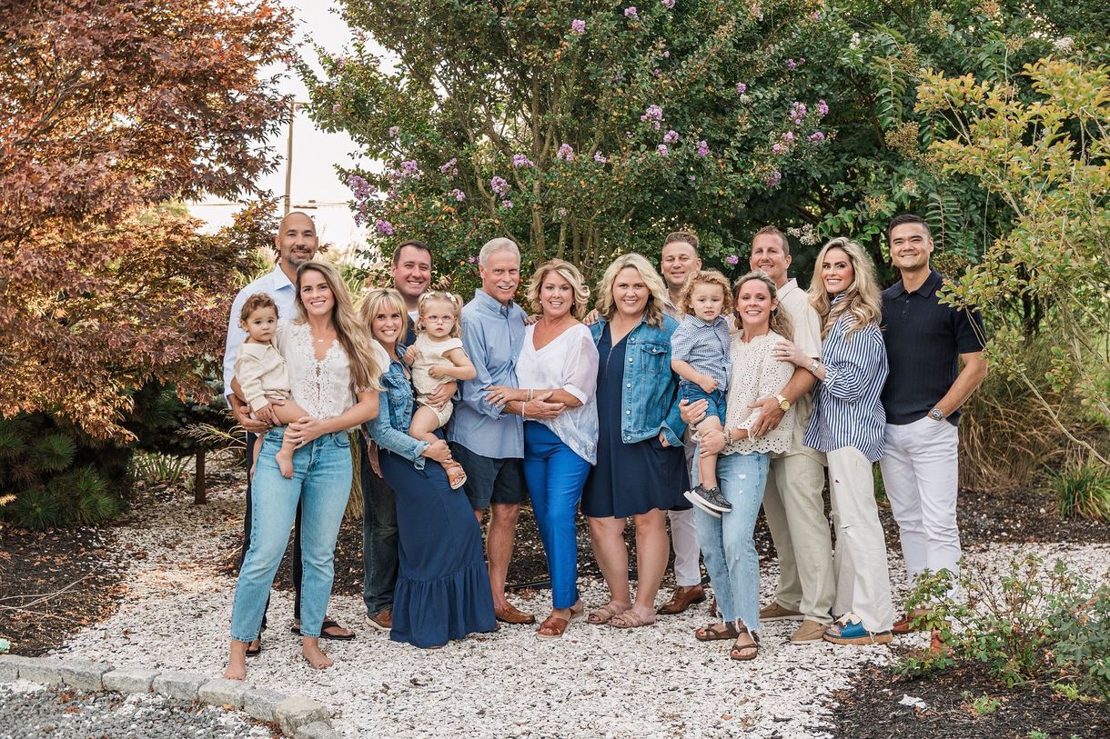 Large family group poses outdoors on a sunny day; various ages, smiles, casual attire.