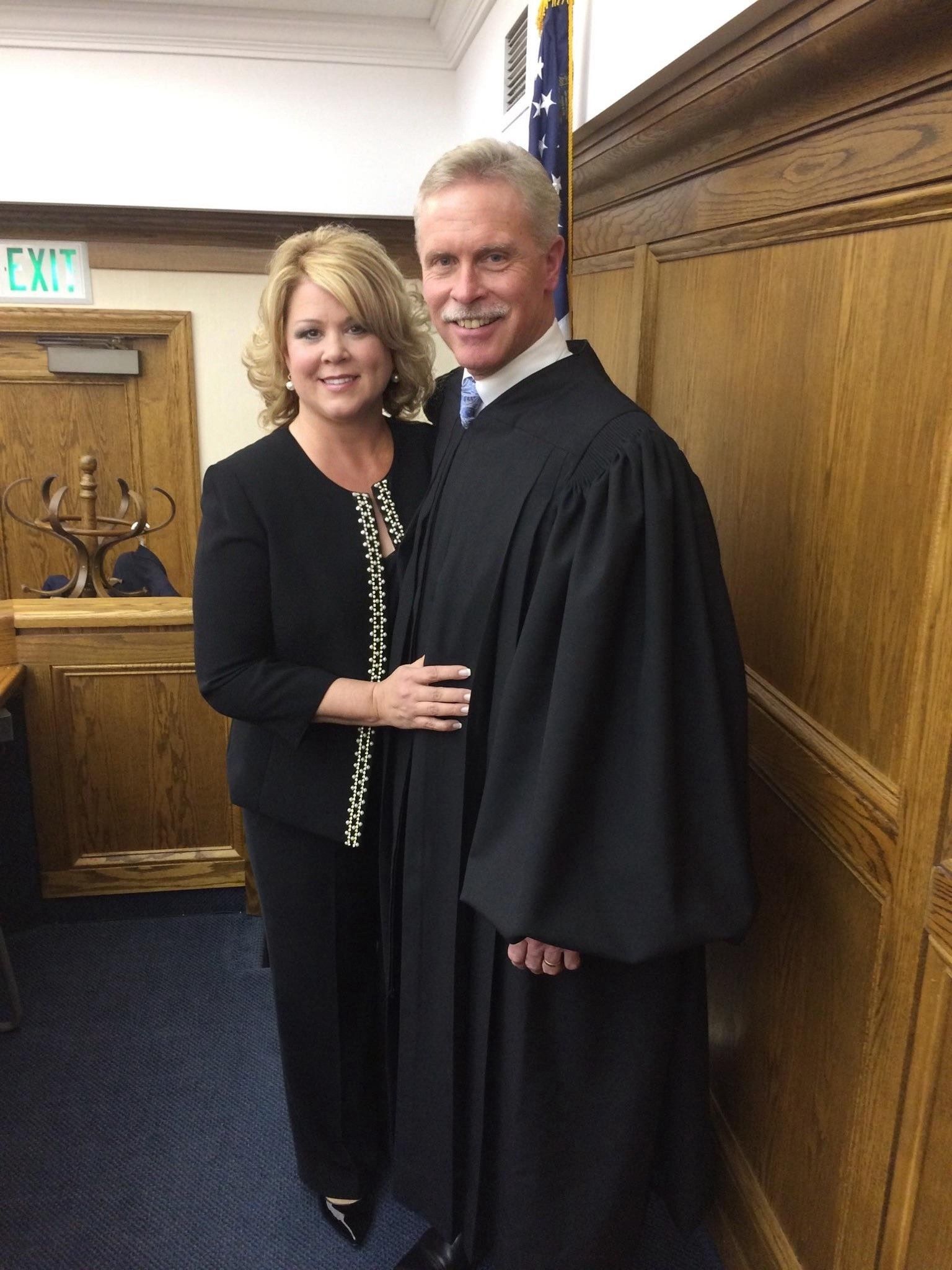 A judge in robes with a woman in a courtroom, smiling.