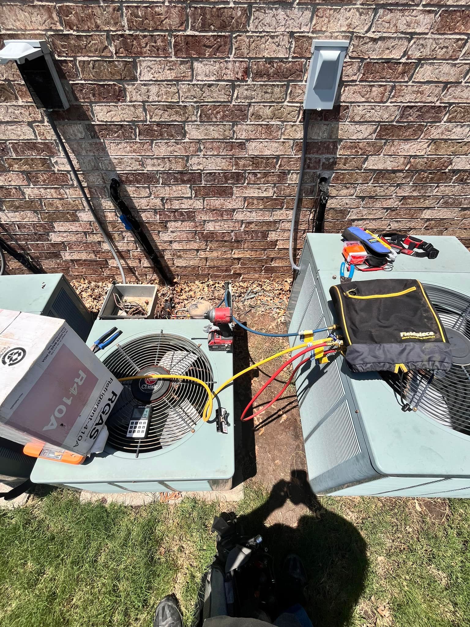 Two air conditioners are sitting next to each other in front of a brick wall.