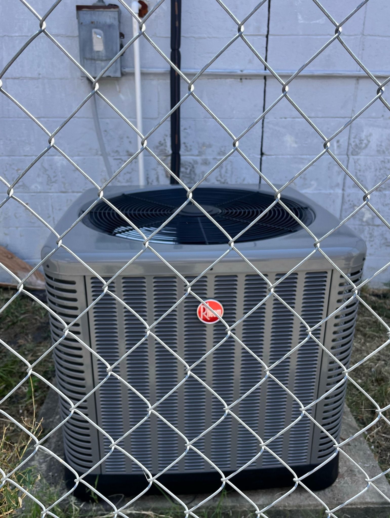 An air conditioner is behind a chain link fence