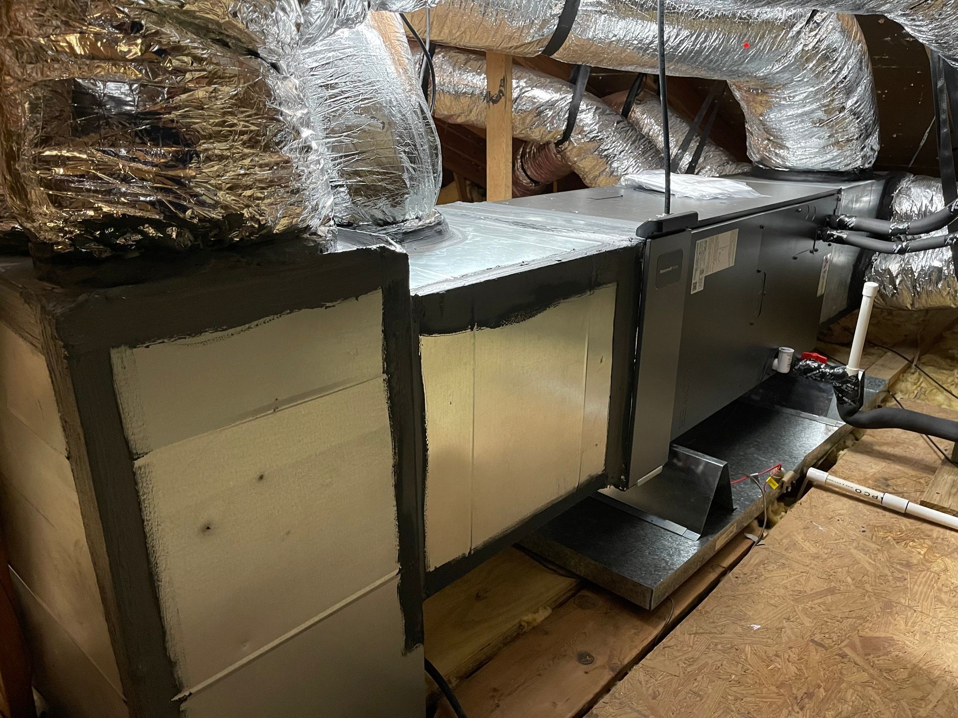 HVAC unit in an attic with insulated ductwork. Silver and gray metal with black insulation.