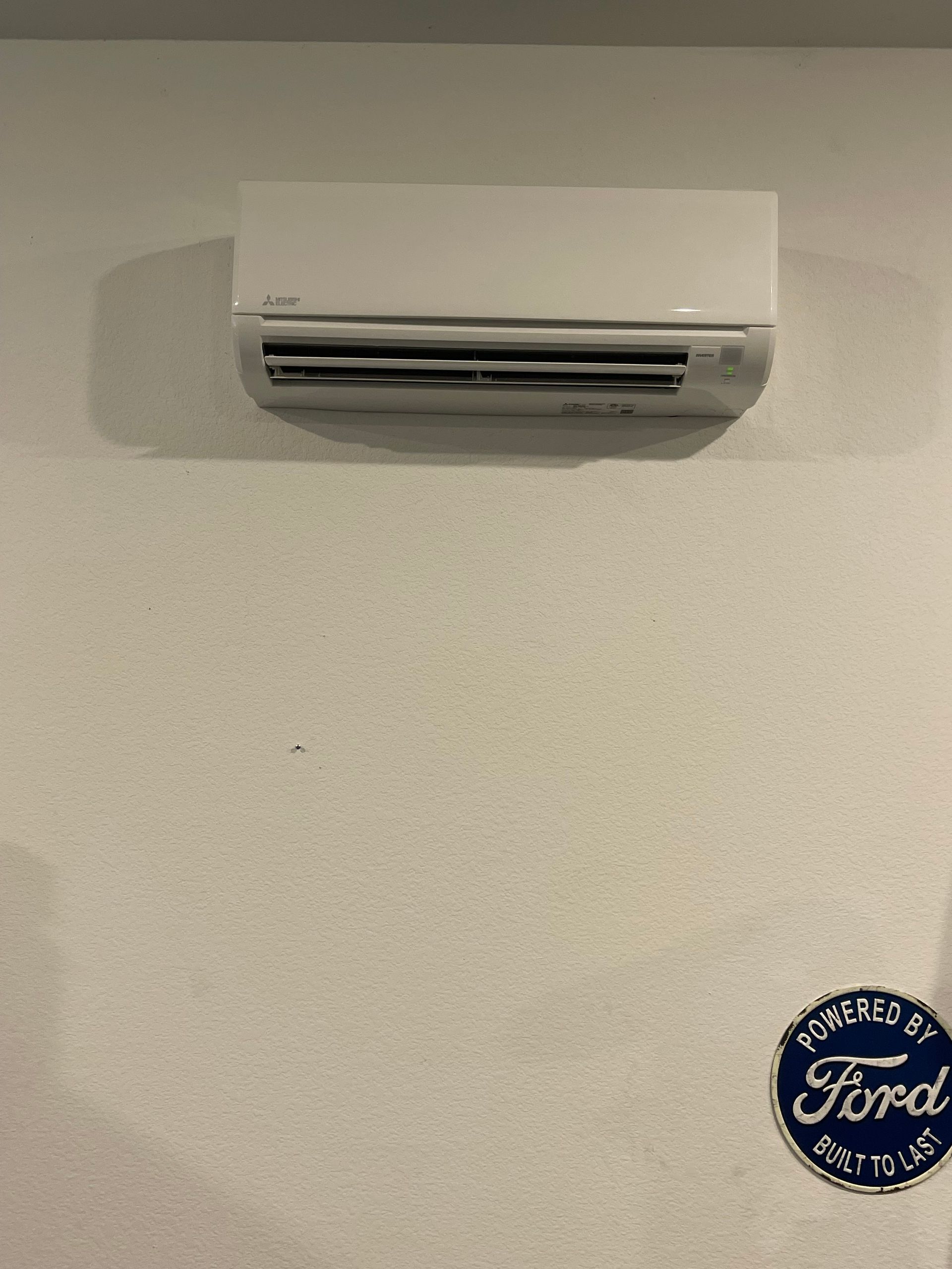 White wall-mounted air conditioner above a Ford logo on a white wall.