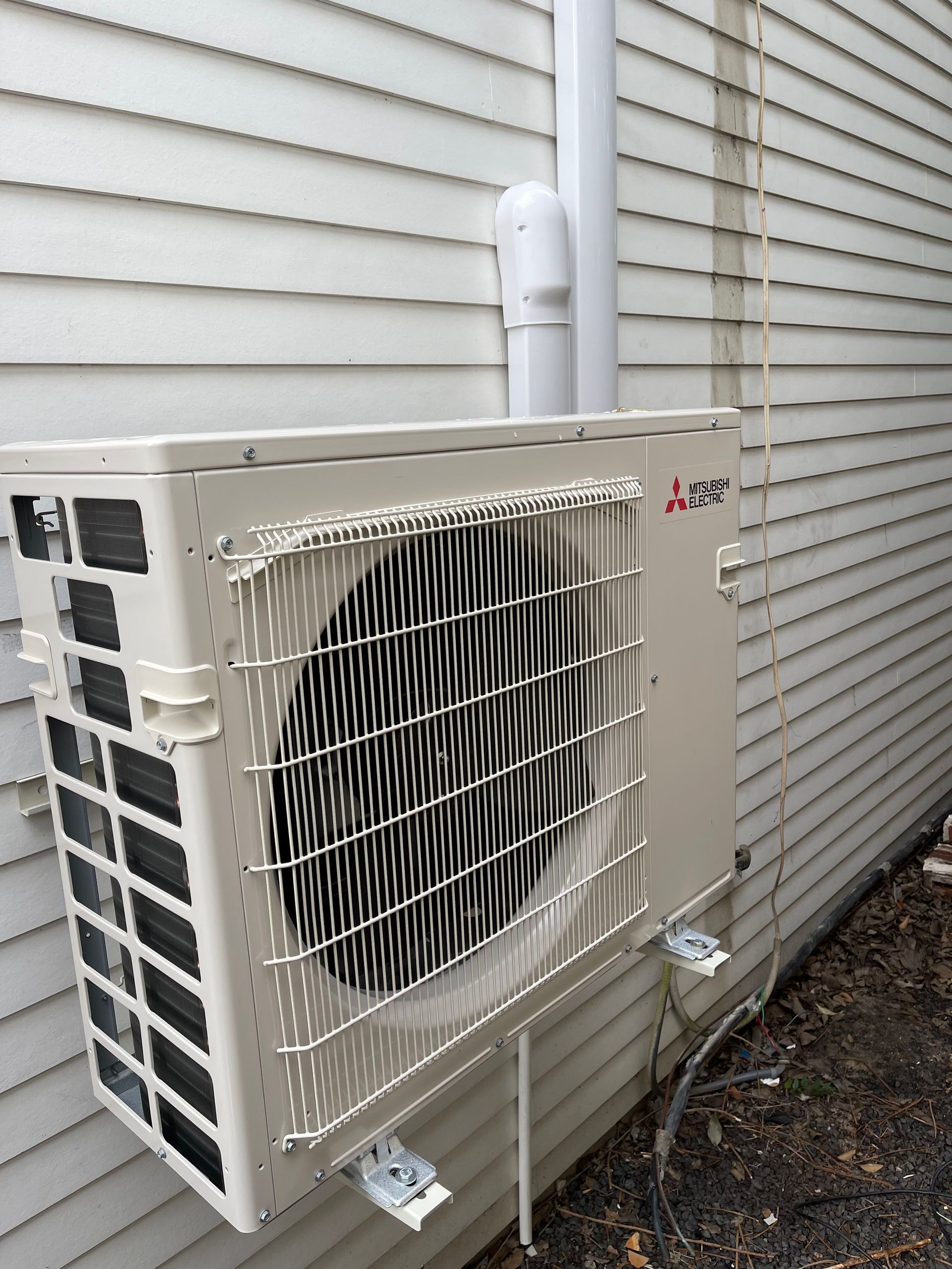 Mitsubishi heat pump unit mounted on a white house exterior with a downspout.
