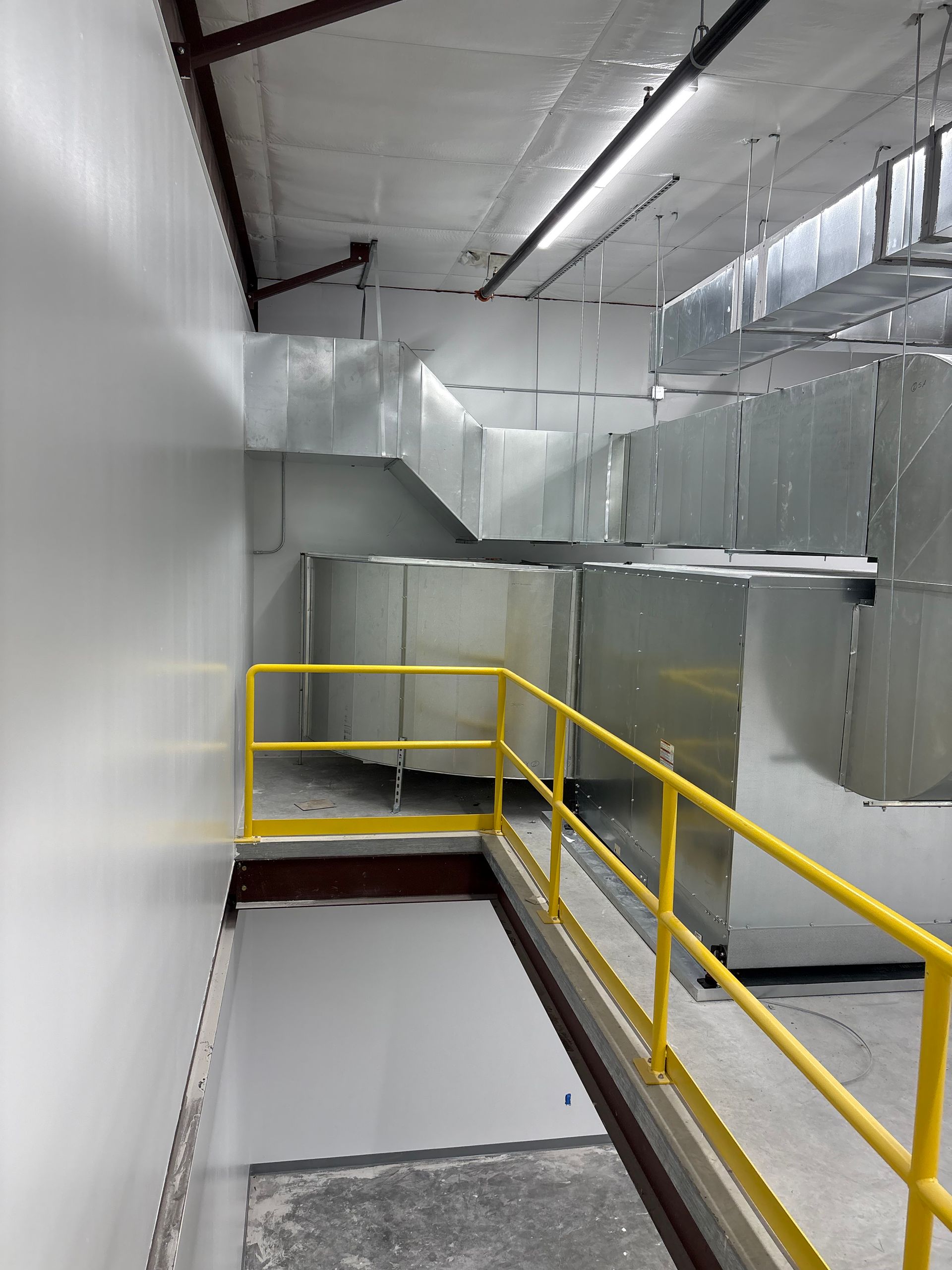 Corridor with yellow railing, metal ductwork, and white walls.