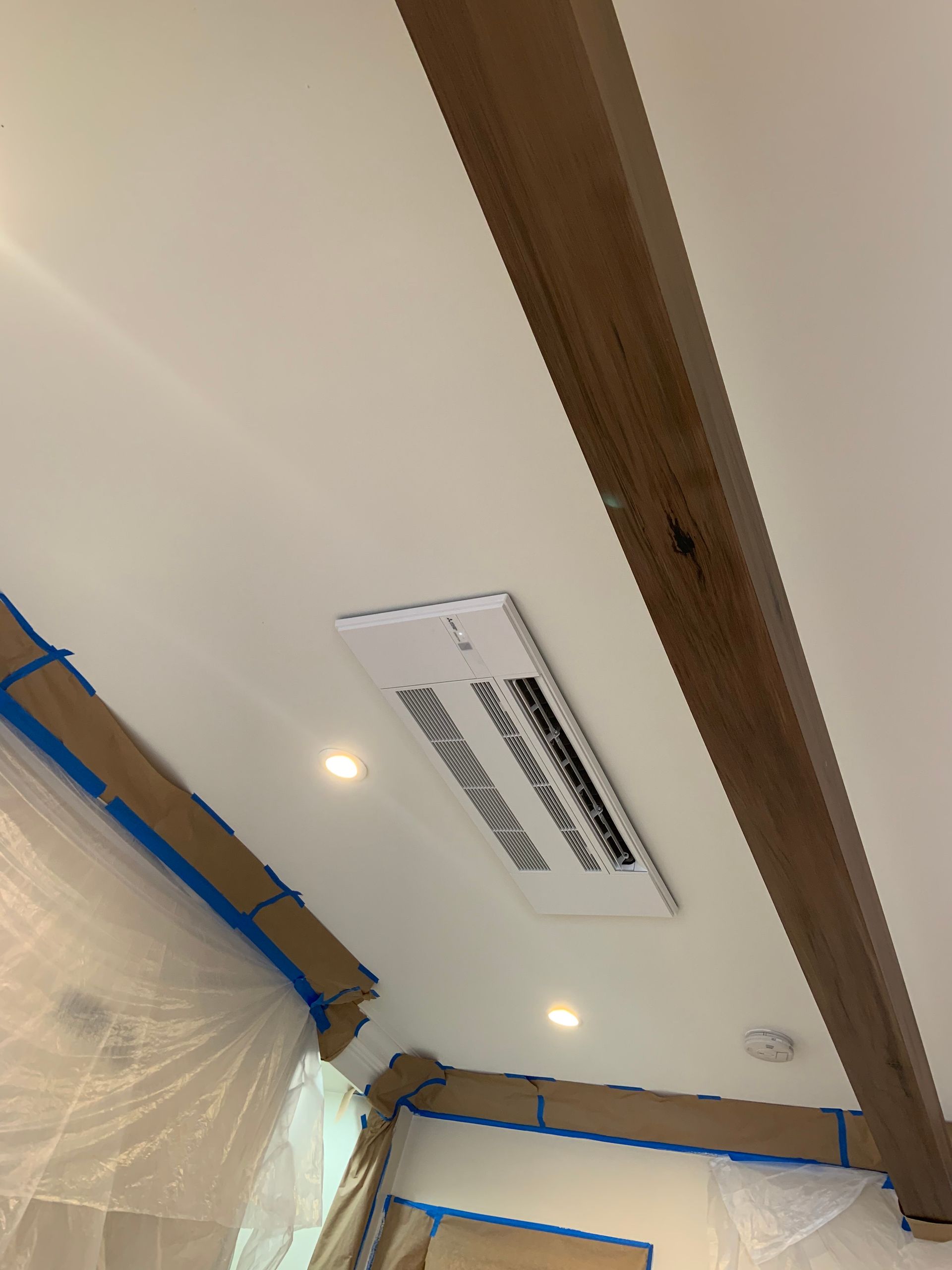 White air conditioner unit mounted on a white wall, near a window. Sunlight illuminates the scene.