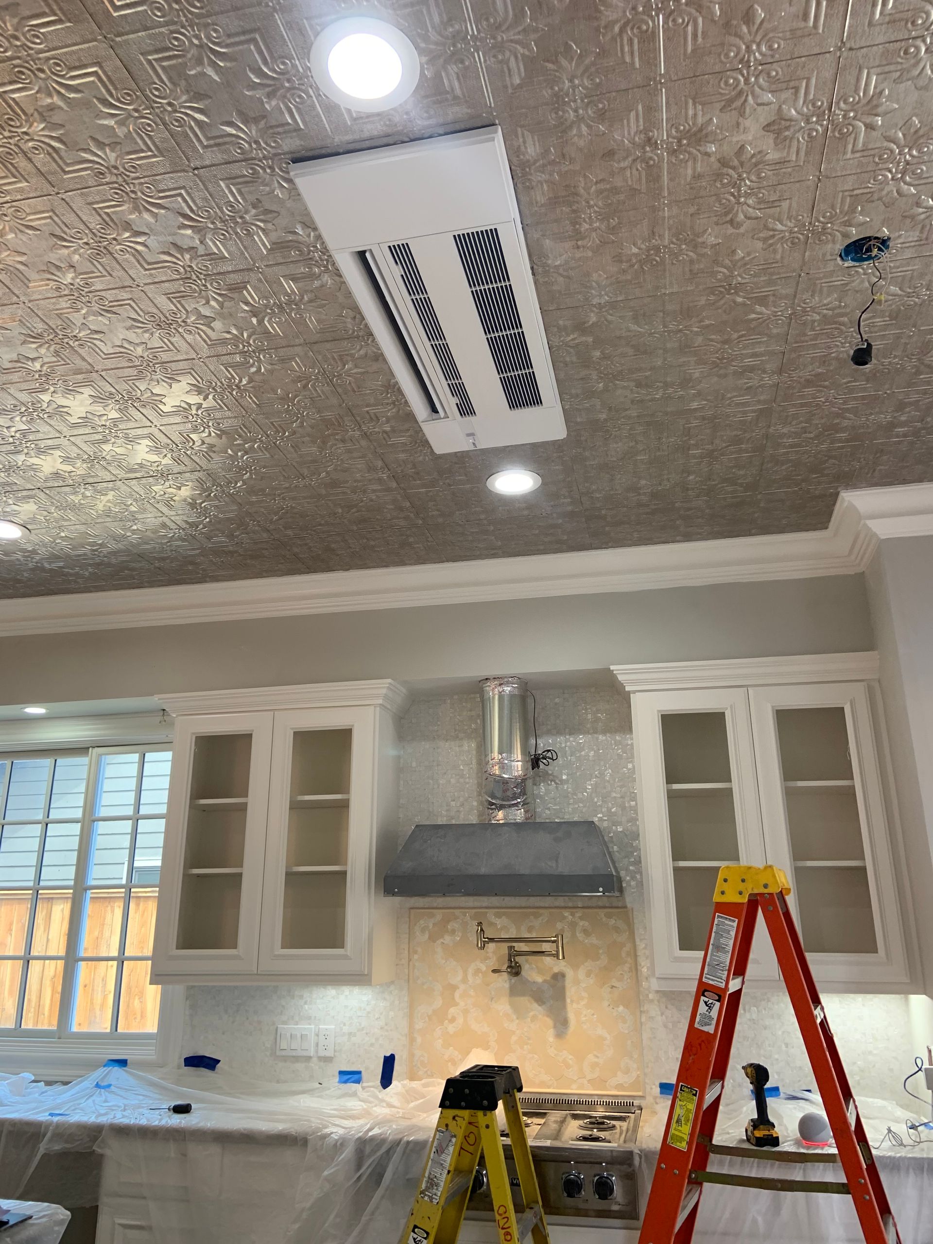 Kitchen under construction with cabinets, ceiling vent, range hood, and ladder.