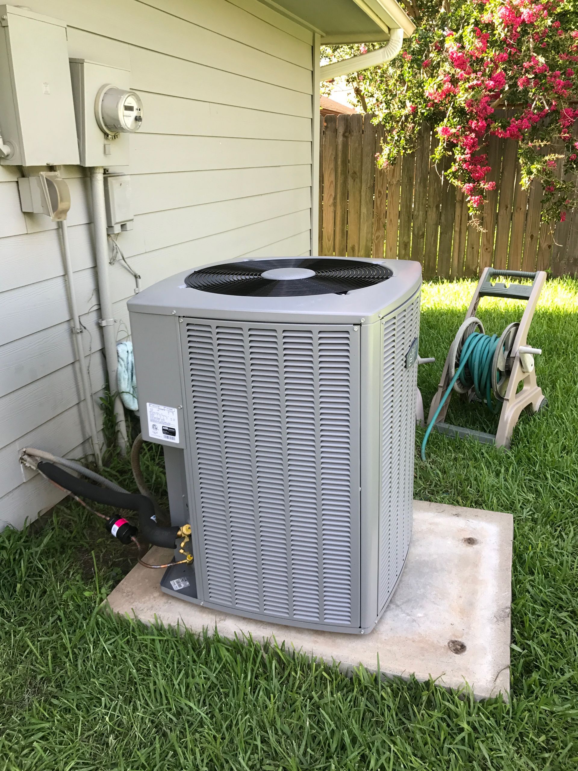 Mitsubishi heat pump unit mounted on a white house exterior with electrical conduit and exhaust pipe.