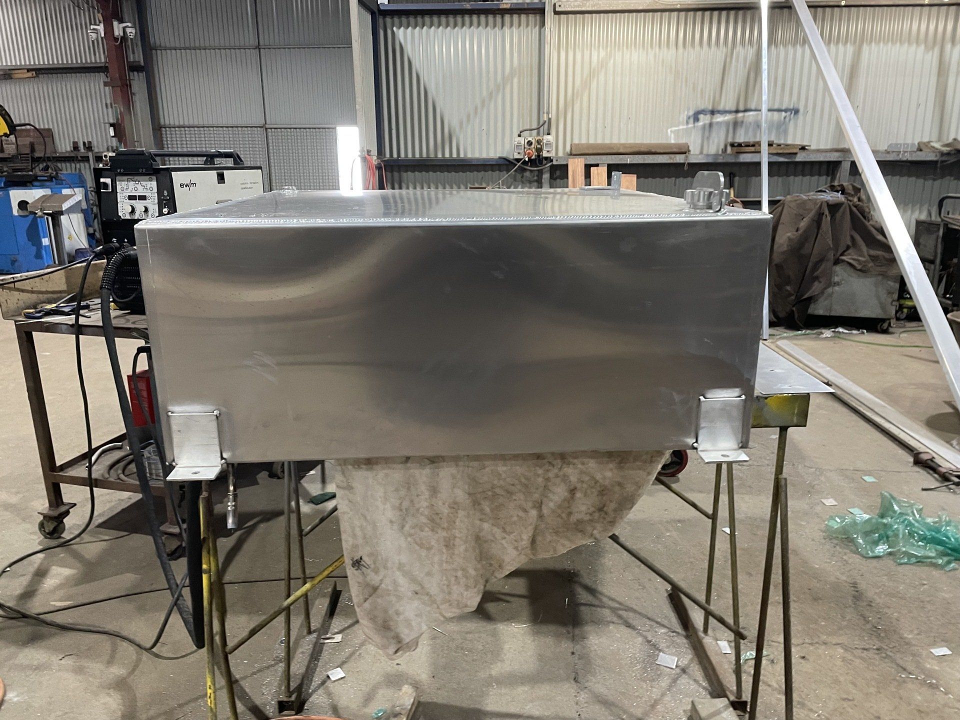 A large stainless steel tank is sitting on a table in a factory.