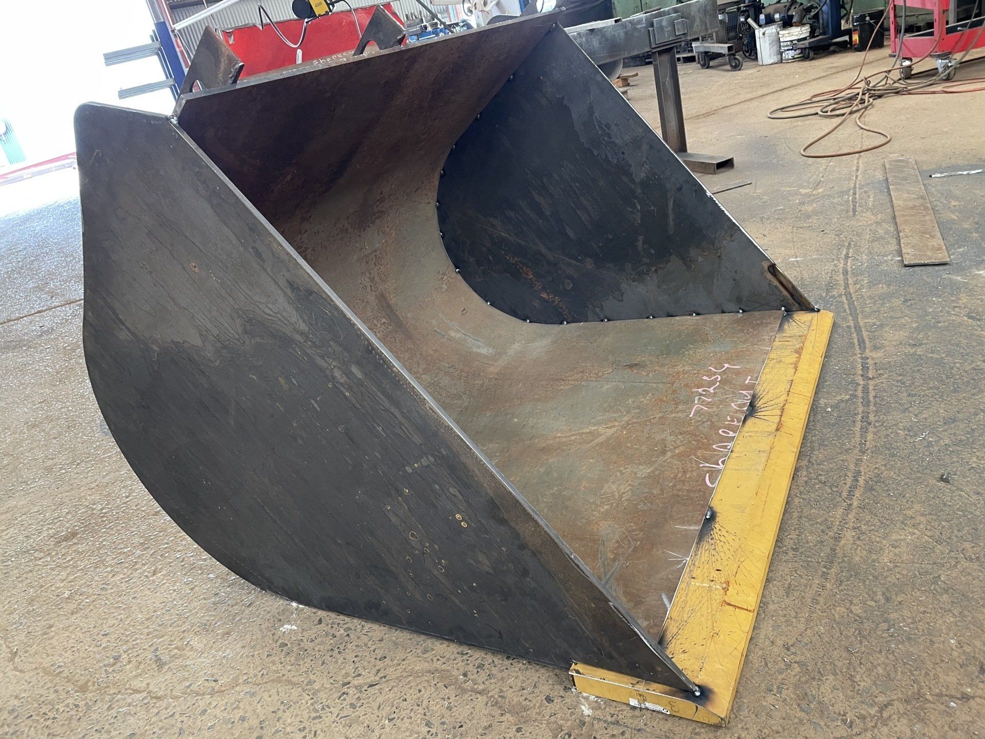 A large metal bucket with a yellow edge is sitting on the ground.
