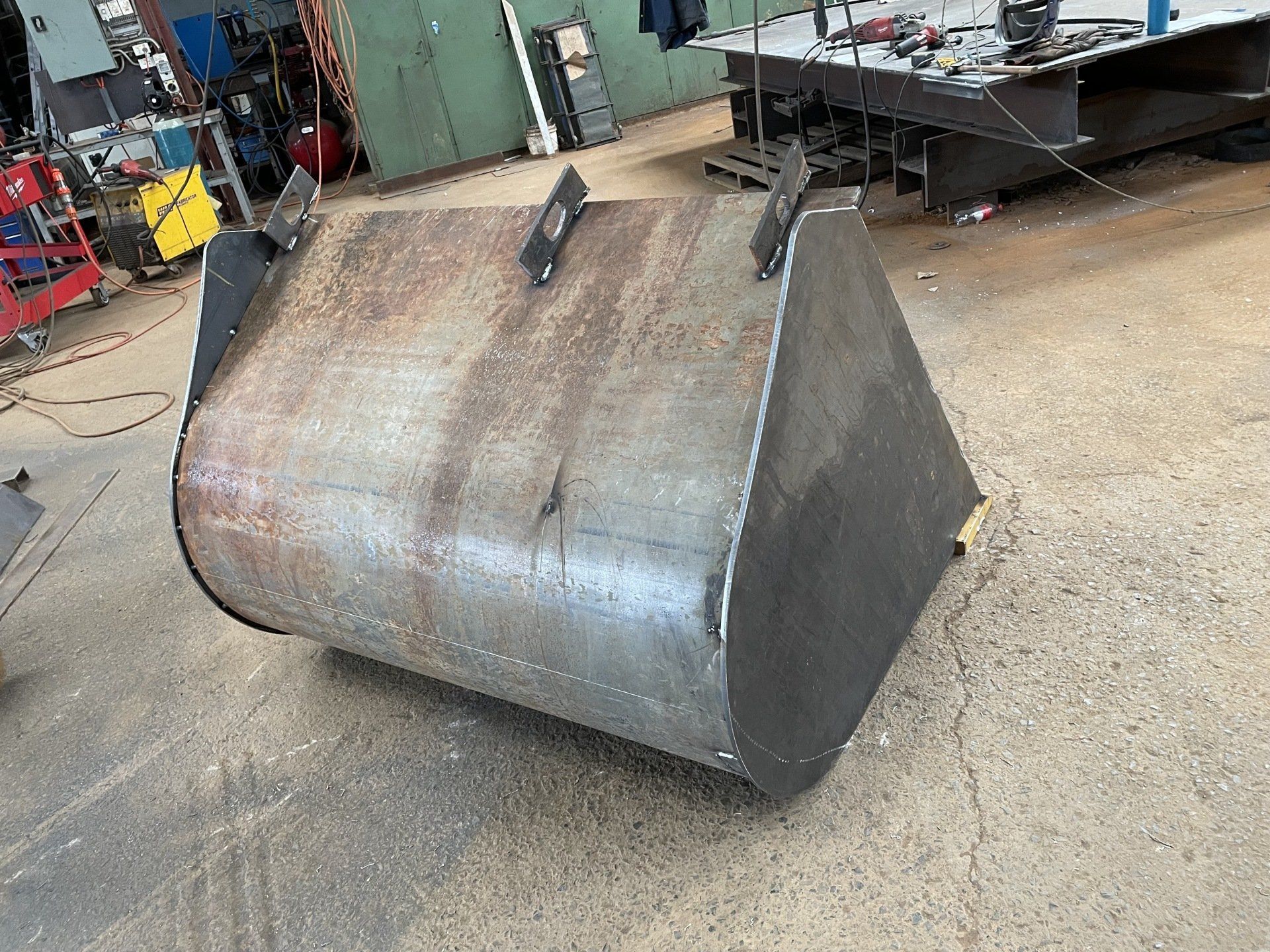 A large metal bucket is sitting on the ground in a factory.