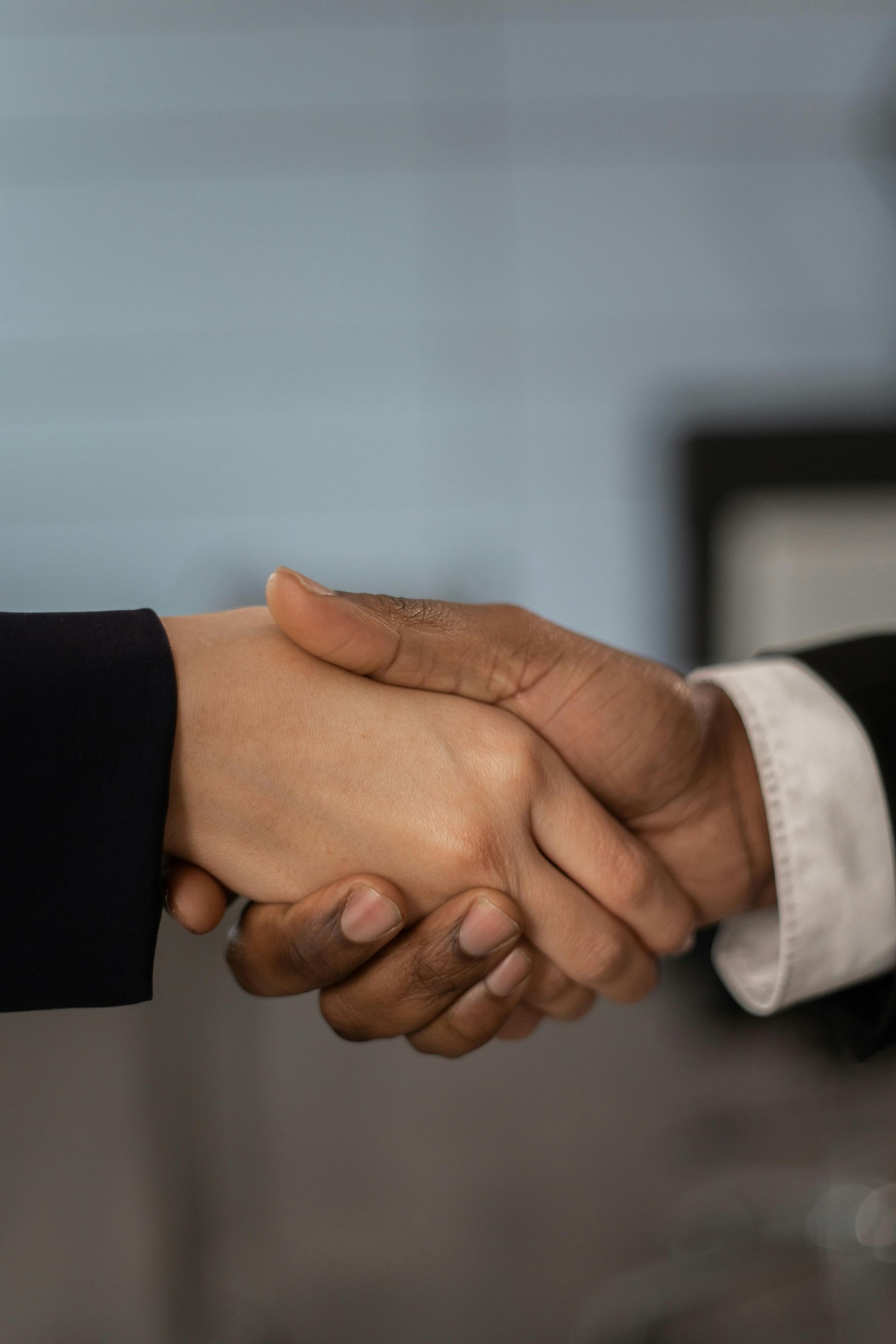 Two people shaking hands, black and white skin, business setting.
